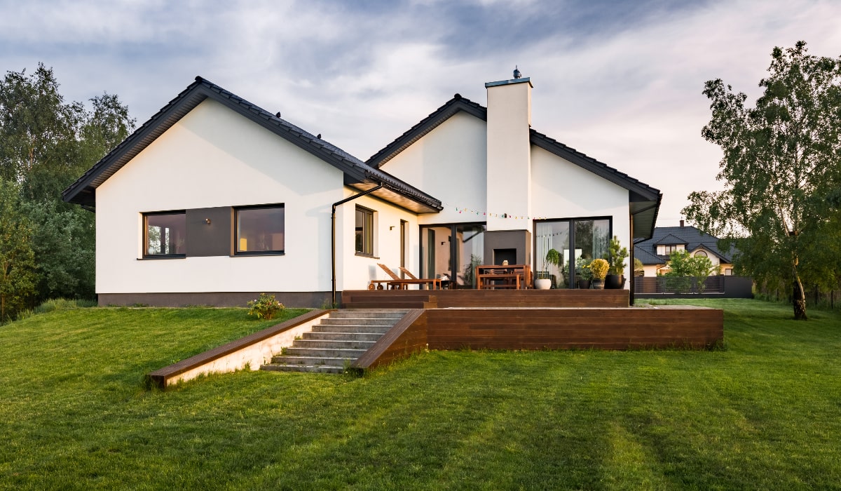 Hvid bolig med terrasse og græsplæne, omgivet af grønne områder klar til en 5 års gennemgang.